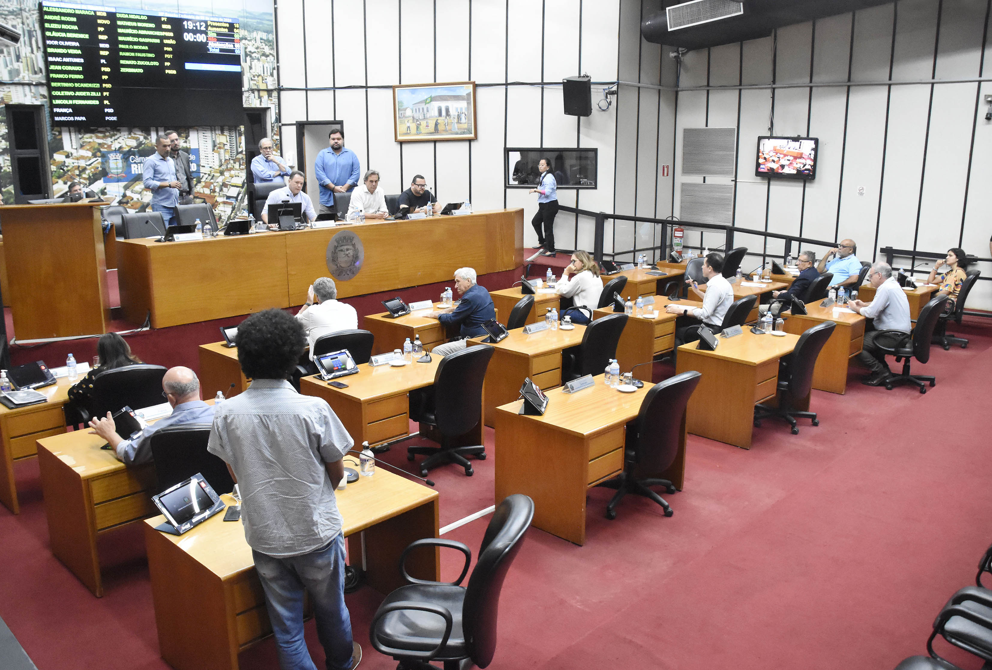 Imagem da Mesa Diretora de frente, com alguns vereadores de costas