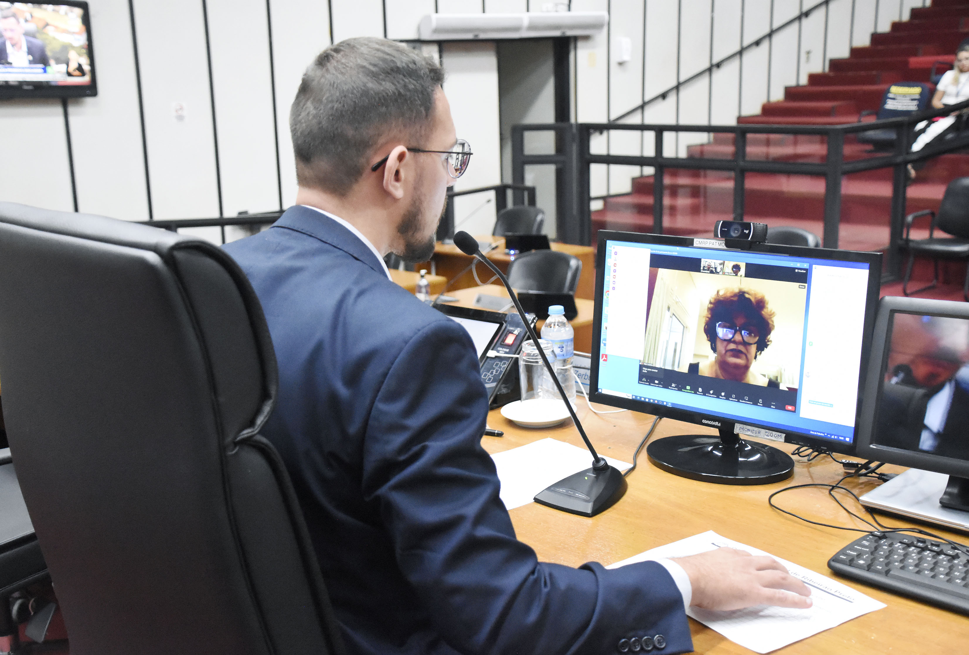 Vereador Zerbinato de costas na foto, de frente para o computador com uma munícipe explanando